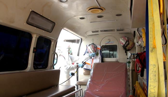 A man in full protective gear disinfects the interior of an ambulance.