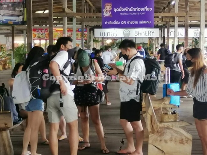 Domestic tourists wearing face masks gather at the Nuanthip Pier in Rayong waiting for ferries to take them to Koh Samed.